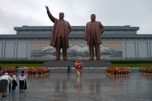Pyongyang, North Korea - August 15 2012: North Koreans showing their respect to their political leaders at the Grand Monument on Mansu Hill with the bronze statues of Kim II Sung and Kim Jong II.