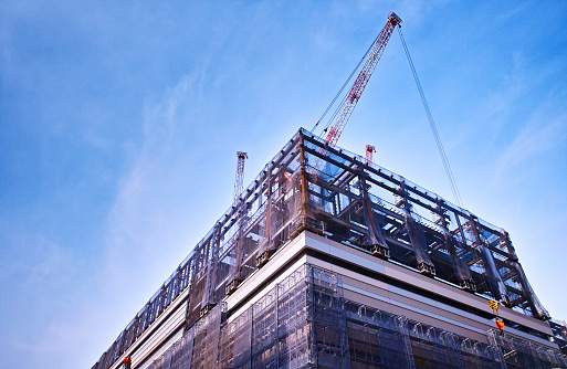 View of a multi-storey hotel under construction and many construction cranes against a cloudy sky,