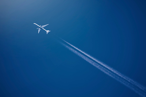 Airliner at high altitude with white condesation trails, on deep blue sky