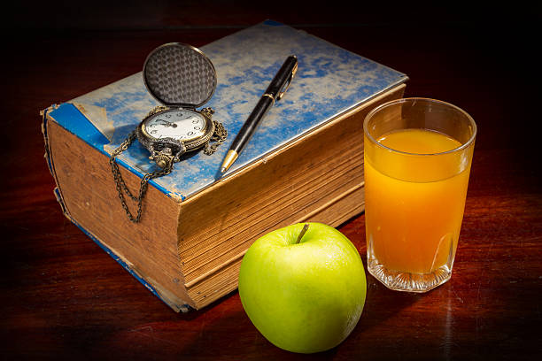 Book with pen,watch apple and orange juice.