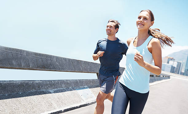 Out running on a beautiful day Shot of two young runners training together on the road off track running stock pictures, royalty-free photos & images