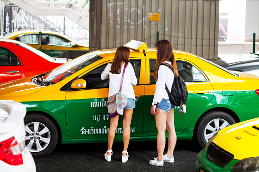 Bangkok, Thailand - March 10, 2016: Two young thai girls are talking to taxi driver while standing in traffic jam on Sukhumvit Road at daytime. Taxi drivers must be asked if they got o wished location or not. Daily checking scene.