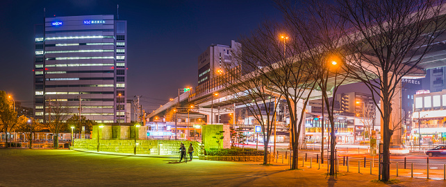 Osaka, Japan - February 26, 2016: Warm lamplight illuminating a group of young women talking beside the elevated highways, train tracks, zooming traffic and crowded skyline of downtown Osaka at night, Japan. Composite panoramic image created from six contemporaneous sequential photographs.