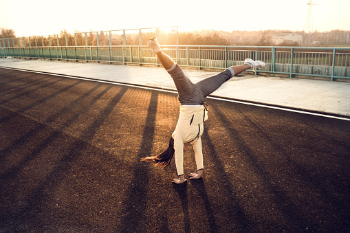 Athletic young woman exercising on the bridge at sunset and doing handstand.