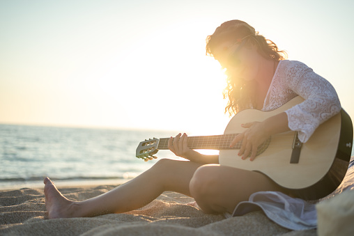 Beautiful woman playing a guitar on the beach at sunset in front the tent.