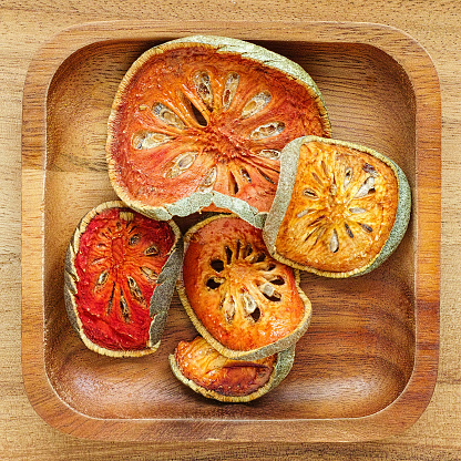 Dried Bael fruit or Aegle marmelos in a wooden tray on a wooden table, this ingredient is used in Indian and other Asian cuisines but commonly it is used mainly in drinks such as teas etc. This image is part of an extensive series of Indian and Asian spices in wooden trays. They can be assembled together to make an attractive ingredient montage design.