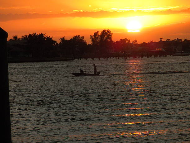 Runing out of daylight. This photo was taken in stuart florida. The sunset was spectactular. You can see that these two guys are leaning foward as if to make the boat go faster and get home before sunset. homeward stock pictures, royalty-free photos & images