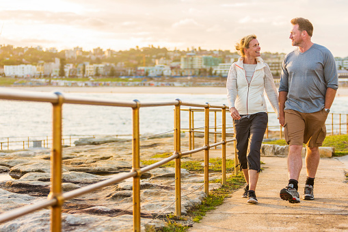 Happy and healthy middle aged active and fit couple walking outdoors by the seaside at Bondi Beach in Sydney, Australia at sunset
