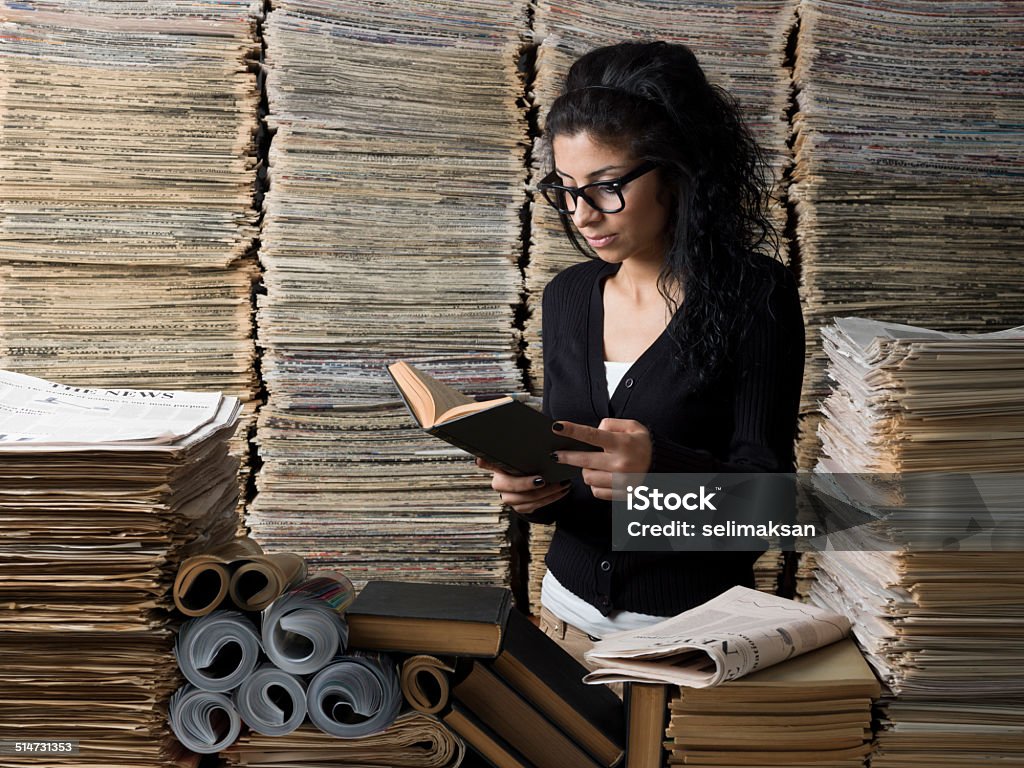 Mixed race female student reading book in library Mixed race female student wearing horn rimmed glasses reading book in library.She has dark hair and brown eyes.She looks at the hard cover book she is holding.The main light is on the left side of frame while model is on the right.The photo was shot in studio with a medium format DSLR camera Hasselblad H4D in horizontal composition. Research Stock Photo