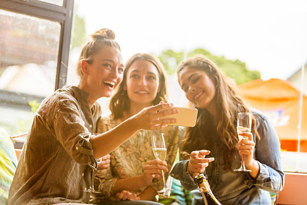 jeunes femmes célébrant et rire avec un téléphone et du champagne - soirée entre filles temps libre photos et images de collection