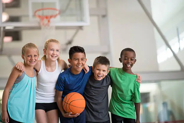 A multi-ethnic group of elementary age children are playing basketball together at the gym during summer day camp.