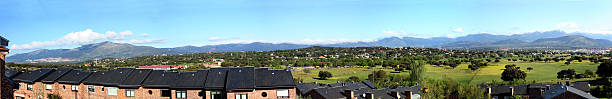 Panoramic view on the Sierra de Guardarrama, a mountain range just North of Madrid, Spain, on a sunny day in early spring. Picture taken from the village of Galapagar. At the far left the El Escorial monestry can be recognised near the mountain foot in the distance; slightly to the right in the first valley, the 150 meter high cross of the Valle de los Caidos monument can be seen.