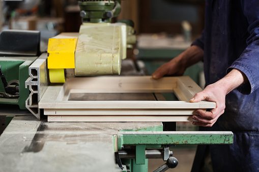 Close up of Carpenter's hands cutting wooden window frame with tablesaw in workshop