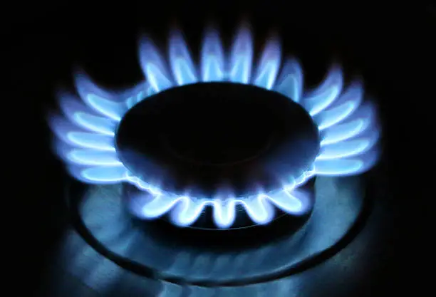 Photo showing glowing blue flame of a gas stove hob. It is possible to see the reflection of the flame in the shiny, black surface of the hob.