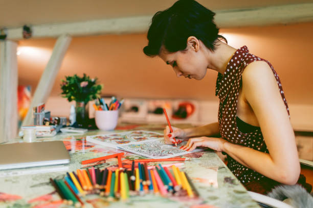 Young smiling woman coloring book for adults in her office or apartment, Enjoy while coloring book for adults. Closed laptop on her desk.