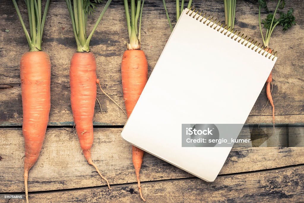 Menu background. Recipe book with fresh carrots on wooden table. Menu background. Recipe book with fresh ripe carrots on wooden table. Vintage color toned image. Cookbook Stock Photo