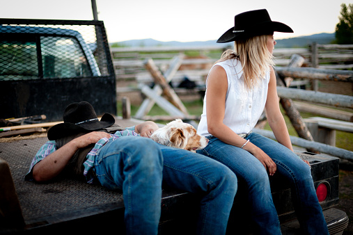 A cowboy and cowgirl relax on the tailgate of a pick-up truck, Parade Rest Ranch, Montana, USA. 