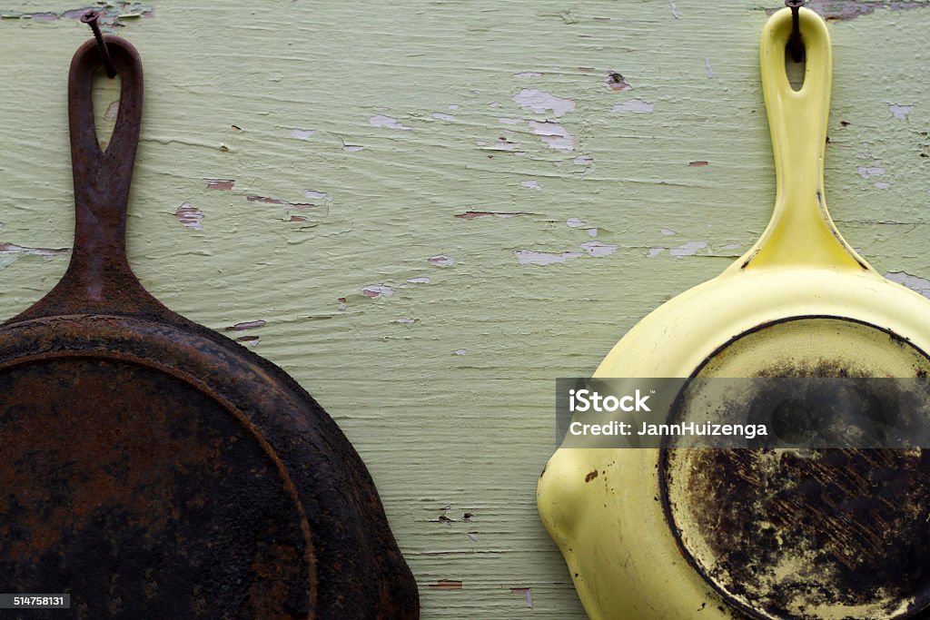 Two Vintage Frying Pans Hanging Against Old Wood Two vintage frying pans hanging from nails on distressed green wood. Frying Pan Stock Photo