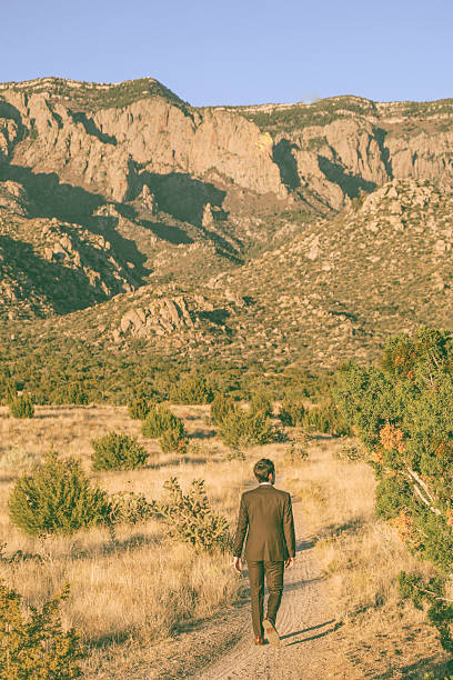 a man wearing a brown suit walks through the desert mountain nature landscape.  vertical composition.