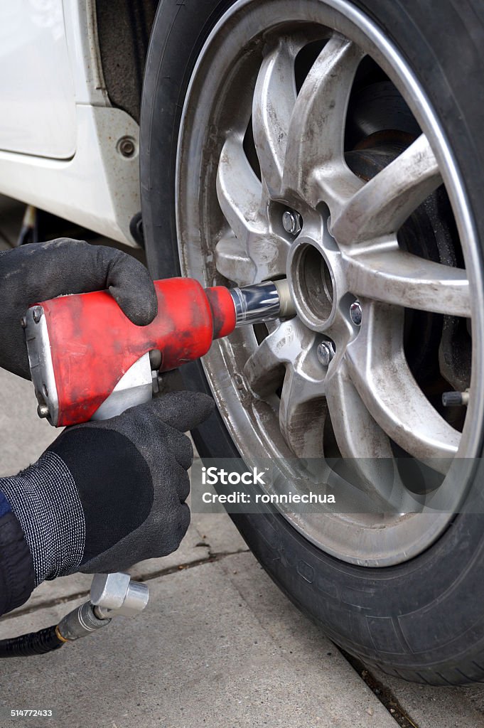 Using Impact Wrench to Change Tires A pair of hands in work gloves holding an air impact wrench to change tires. Impact Stock Photo