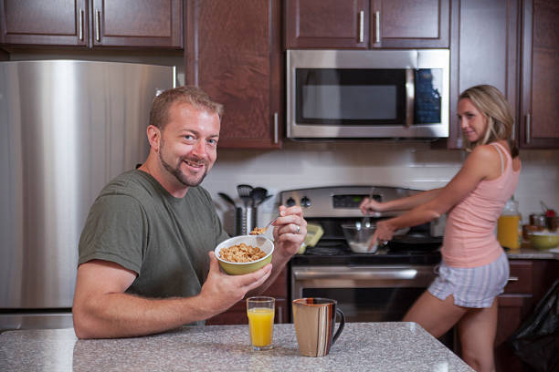 Uomo mangia cereali, mentre il lady rende la prima colazione - foto stock
