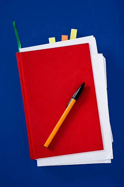Red notebook with pen on navy-blue background