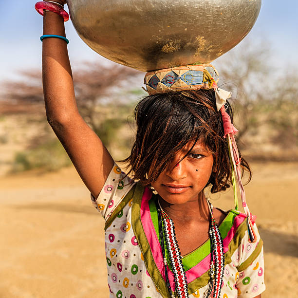 indische mädchen tragen von wasser auf ihrem kopf aus gut - poverty india child little girls stock-fotos und bilder