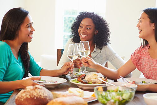 Group Of Female Friends Enjoying Meal At Home Making A Toast With Wine