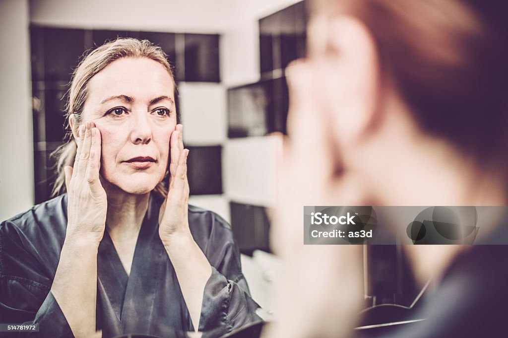 Mature Woman putting cream on her face Mirror - Object Stock Photo