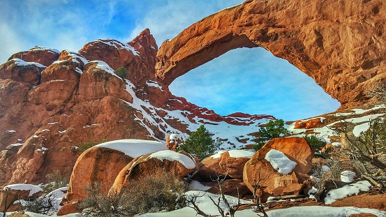 Picturesque Winter Morning with blue sky and some clouds. Snow is still spotted on the ground around one of the north and south Windows Spectacles Arch, in the Windows District of Arches National Park, Utah.