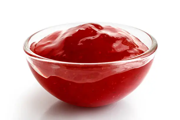 Small glass ramekin of red strawberry jam isolated on white, in perspective.