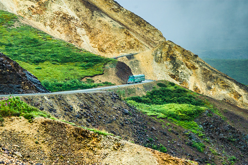 A National Park bus (center) drives down a steep, unguarded mountain road as it transports visitors through the extensive Denali National Park.