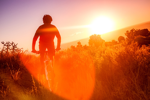 man riding mountain bike silhouetted against sunshine lens flare while riding in the desert landscape of the sandia mountains.  horizontal composition.