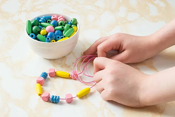 Children's hands to collect different colored wooden beads on a string