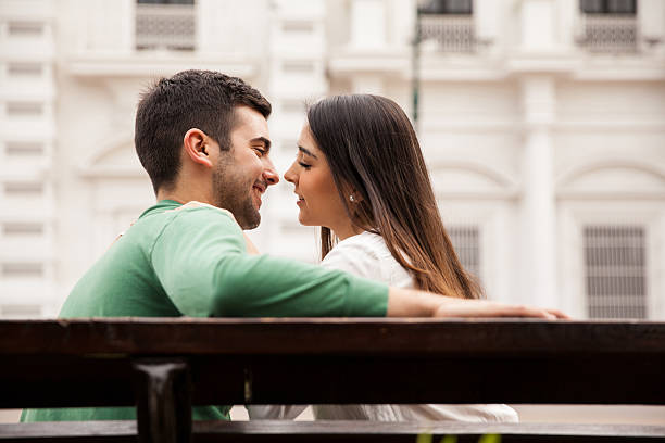 Rear view of a young couple in love sitting on a park bench and about to kiss