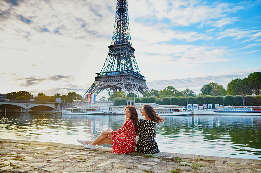 Beautiful twin sisters in red and black polka dot dresses in front of the Eiffel tower near the river Seine in Paris, France