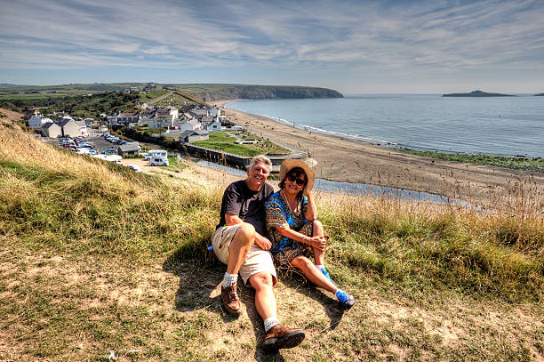 istock Mature smiling couple sitting on grassy headland overlooking beach 514825163