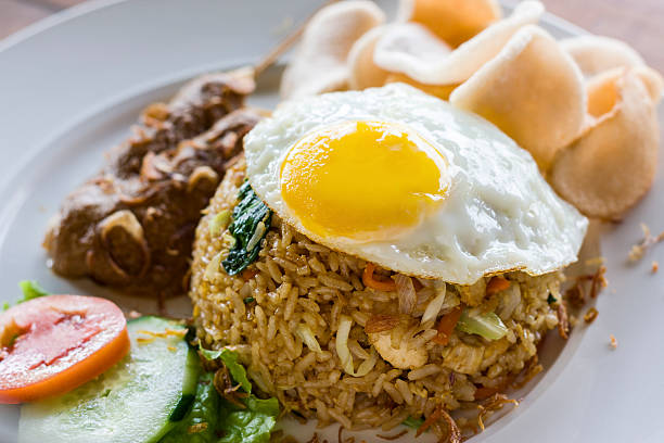 Nasi Goreng indonesian fried-rice dish with egg and chicken satay A popular fried rice dish in Indonesia and Malaysia. Served with egg, chicken satay, prawn crackers and salad garnish. indonesian culture photos stock pictures, royalty-free photos & images