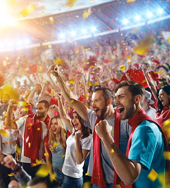 Sport fans: Happy cheering friends On the foreground a group of cheering fans watch a sport championship on stadium. Everybody are happy. People are dressed in casual cloth. Colourful confetti flies int the air. football fans in stadium stock pictures, royalty-free photos & images