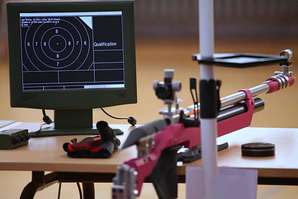 A used paper shooting target, silhouetted as a human torso, is affixed to a plain gray wall. The target displays multiple bullet holes concentrated heavily around the central bullseye and chest area.