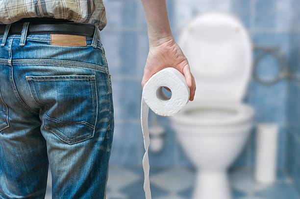 Man suffers from diarrhea holds toilet paper roll Man suffers from diarrhea holds toilet paper roll in front of toilet bowl. domestic bathroom stock pictures, royalty-free photos & images