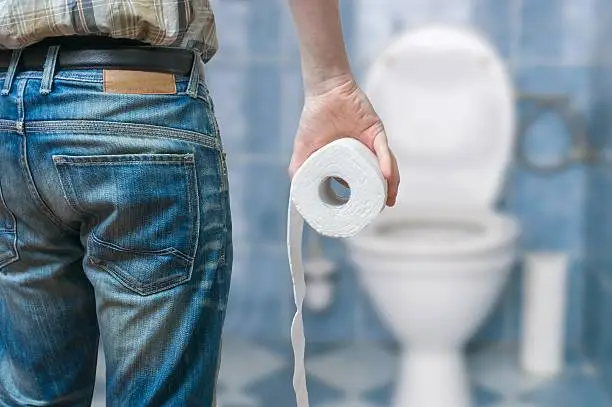 Man suffers from diarrhea holds toilet paper roll in front of toilet bowl.