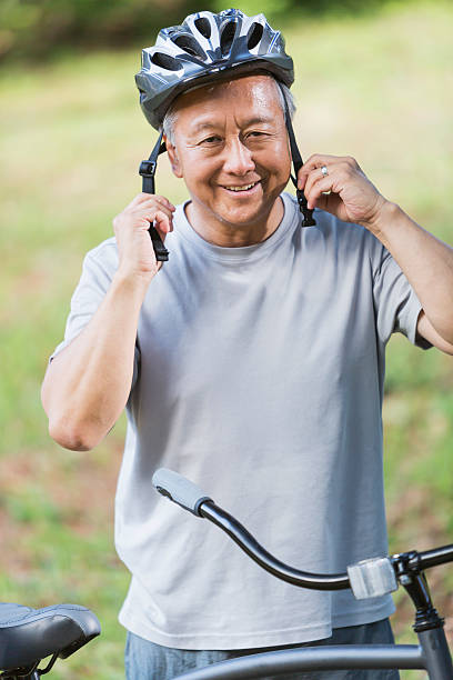 hombre asiático putting en bicicleta casco - cycling senior adult sports helmet men fotografías e imágenes de stock