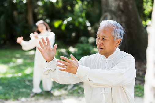 Senior Asian couple (60s) practicing Tai Chi.  Focus on man.