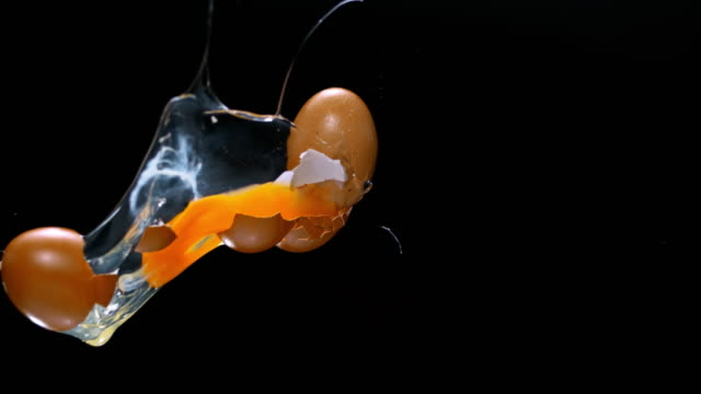 SLO MO ETwo eggs hitting each other in the air on black background