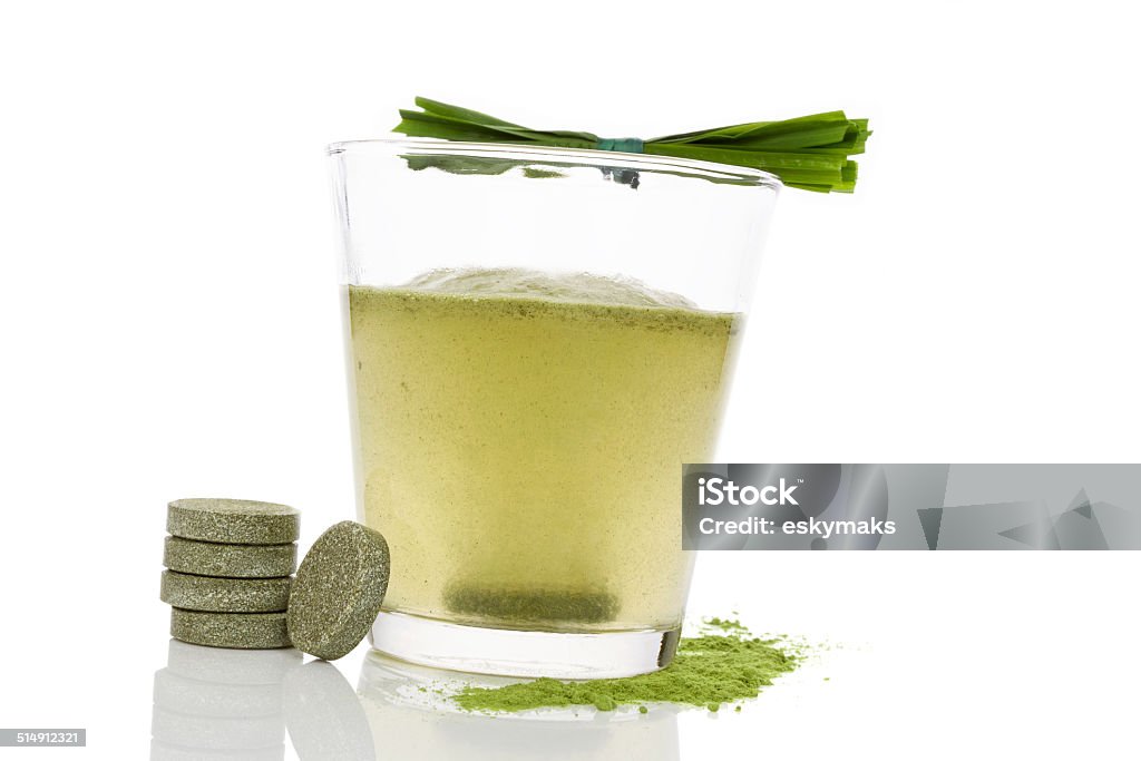 Detox. Glass with dissolving effervescent green tablet, grass blades and green ground isolated on white background. Chlorella, spirulina and wheat grass. Alternative Medicine Stock Photo