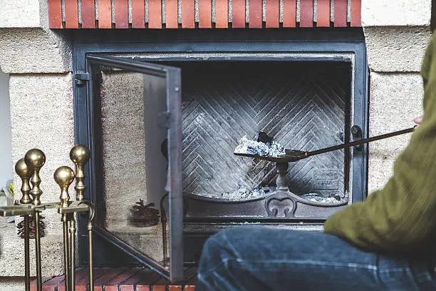 A man cleans the fireplace. Taken out of the fire a long-handled shovel with ash