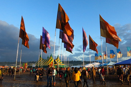 Glastonbury, United Kingdom - June 27, 2014: Crowds trek through the mud beneath brightly colored flags after a rainstorm at Glastonbury Festival in Somerset, England.