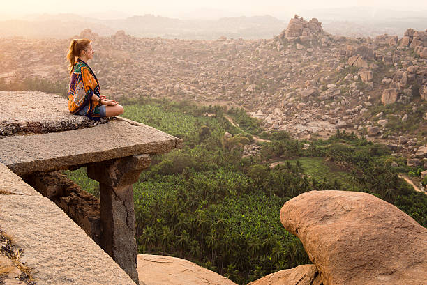 Young woman meditating on mountain cliff on sunrise in Hampi, India. Copy space