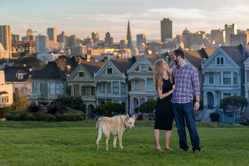 Couple  have a shoot at Classic Victorian houses across the street from Alamo Square in San Francisco. Skyline of San Francisco is seen in background.